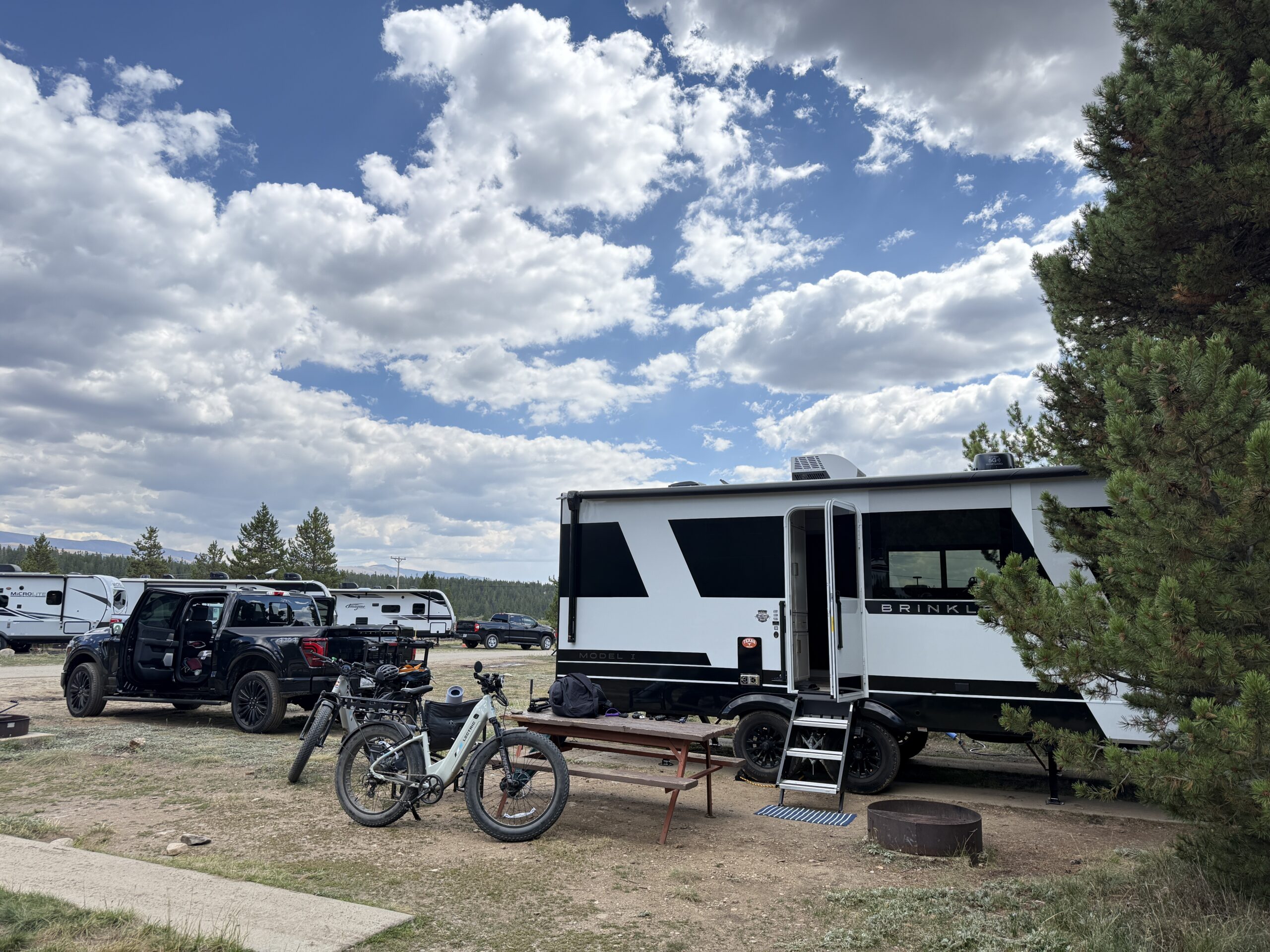 The Brinkley trailer at a Leadville campground with two e-bikes, a picnic table and pine trees.