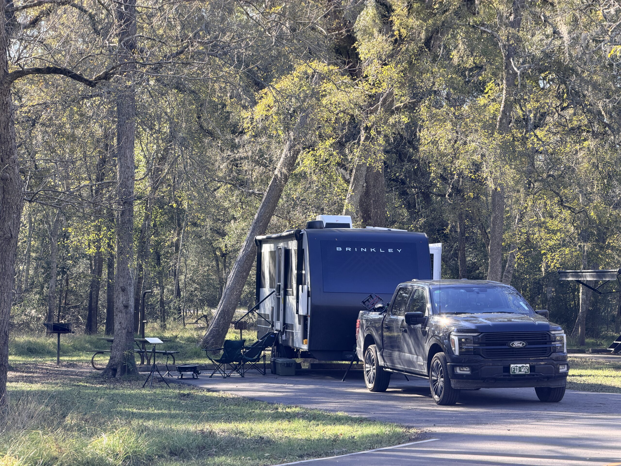 Black Brinkley travel trailer and Ford pickup parked at a wooded campsite in Brazos Bend State Park.