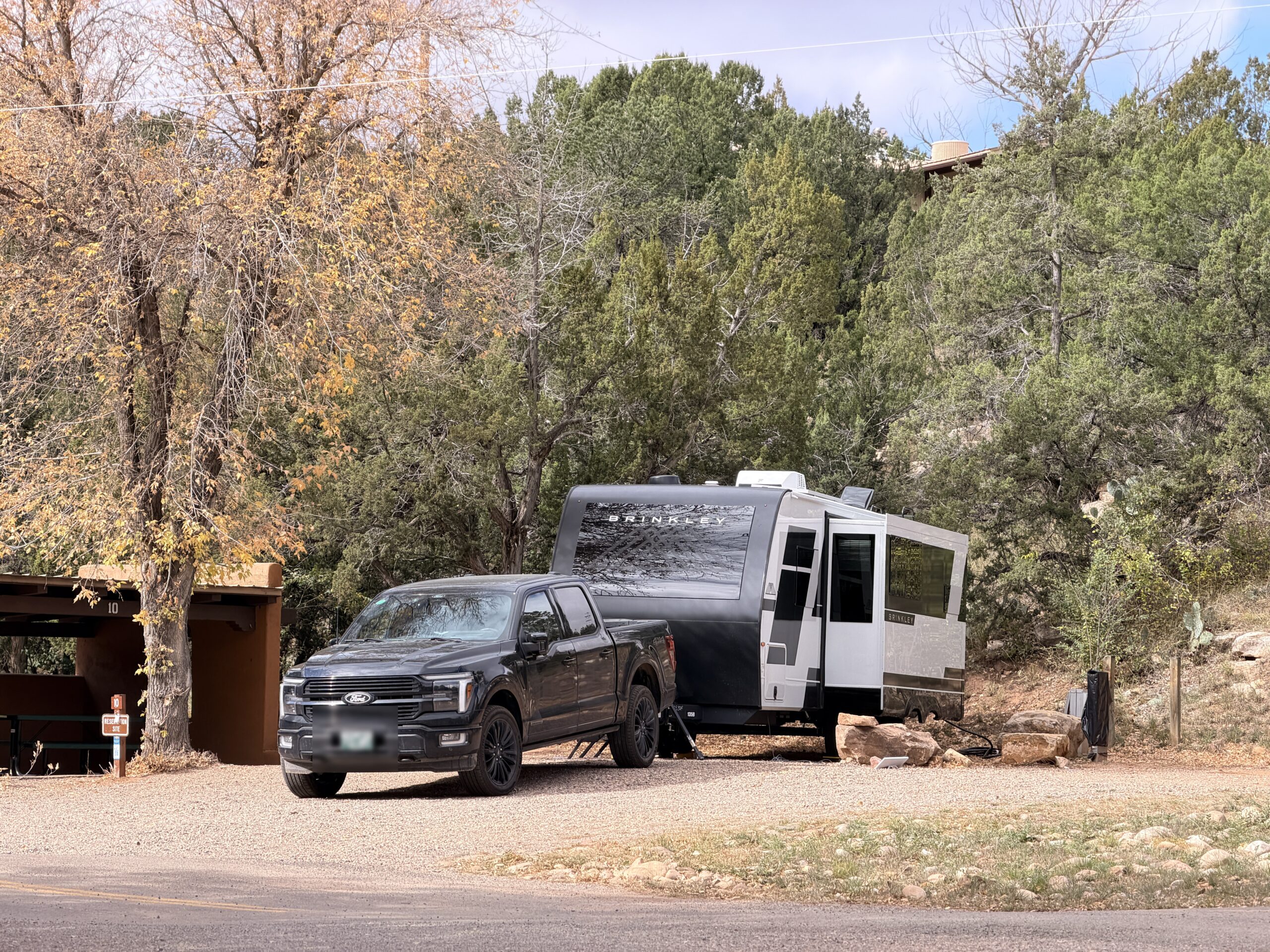 The Brinkley trailer and black Ford pickup at a gravel site among junipers and fall trees at Villanueva.