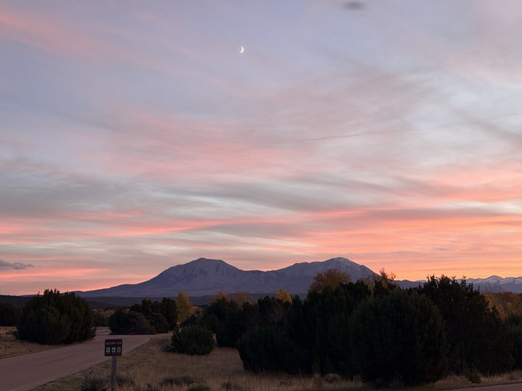 A crescent moon above pink streaked clouds over the Spanish Peaks near Lathrop State Park.