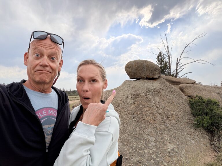 Matt and Erin pulling surprised faces and pointing at a balanced boulder