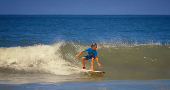 Young surfer in a blue rash guard riding a wave in Tamarindo, Costa Rica.