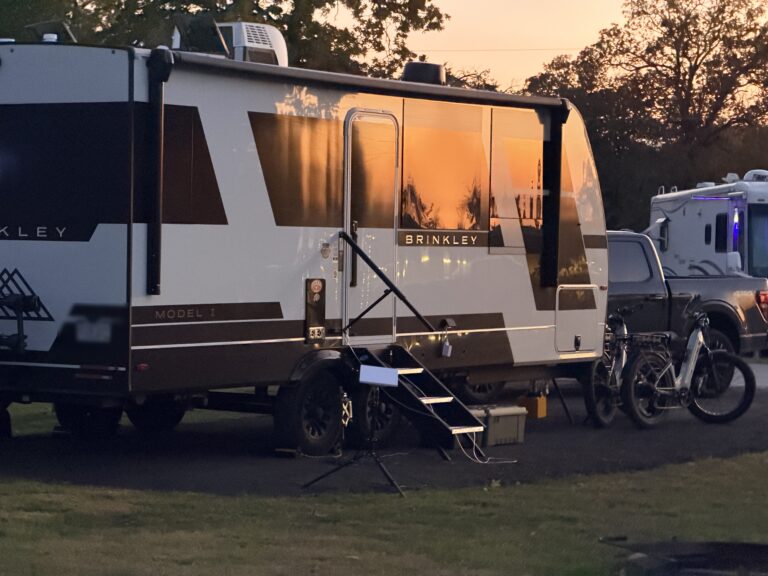 Brinkley Model I travel trailer at a campsite with sunset light reflecting in its windows and e-bikes beside it.