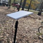 Starlink Mini dish on a tripod stand at a leaf-covered campsite beside the power pedestal.