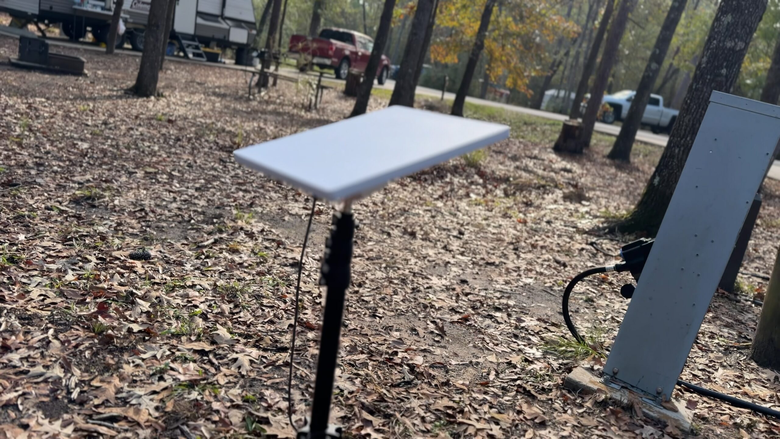 Starlink Mini dish on a tripod stand at a leaf-covered campsite beside the power pedestal.